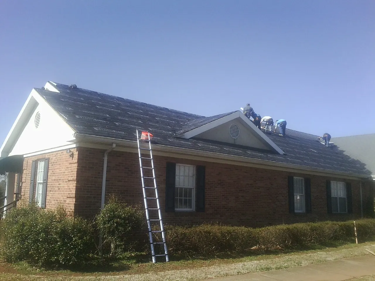 Crew tearing shingles off a brick ranch roof with a ladder set — Emergency Roof Repair work by our crew in Colfax